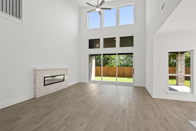 unfurnished living room with a high ceiling, a fireplace, ceiling fan, and hardwood / wood-style flooring