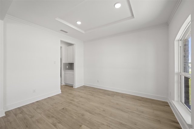 unfurnished room featuring a raised ceiling, crown molding, and light hardwood / wood-style flooring