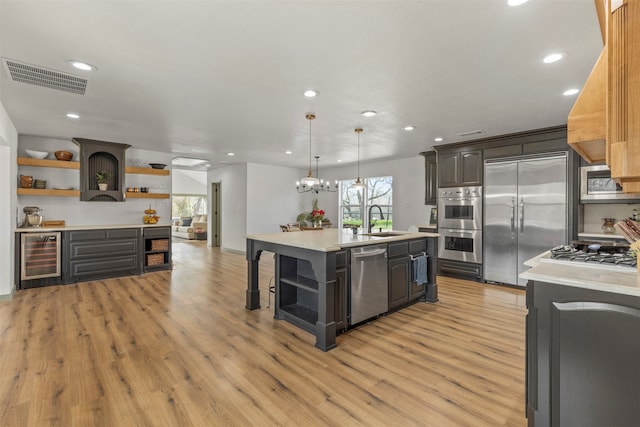 kitchen with light hardwood / wood-style flooring, a center island with sink, sink, beverage cooler, and appliances with stainless steel finishes