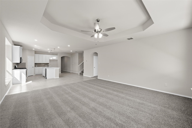 unfurnished living room featuring a tray ceiling, ceiling fan, light colored carpet, and sink