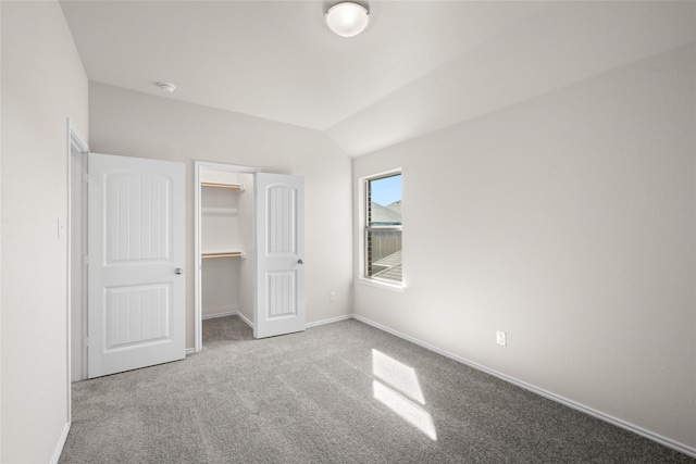 unfurnished bedroom featuring carpet, lofted ceiling, a walk in closet, and a closet