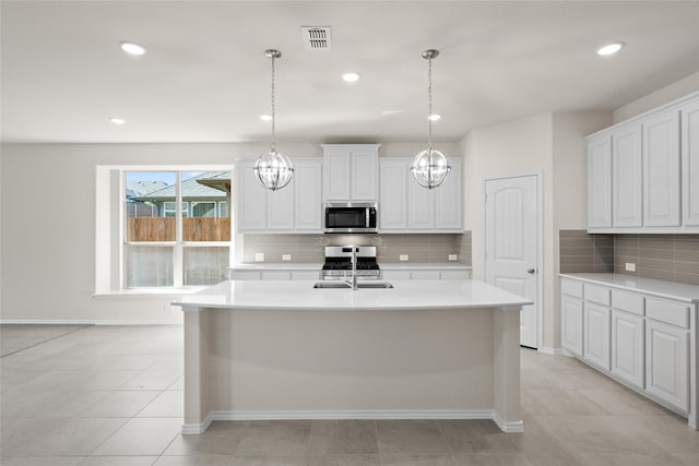 kitchen featuring a kitchen island with sink, hanging light fixtures, white cabinets, and stainless steel appliances