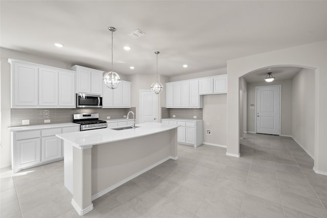 kitchen featuring appliances with stainless steel finishes, hanging light fixtures, an island with sink, sink, and white cabinetry