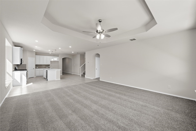 unfurnished living room featuring ceiling fan, sink, a raised ceiling, and light colored carpet