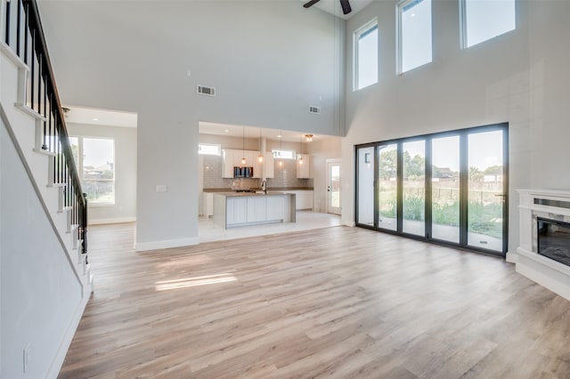 unfurnished living room with ceiling fan, sink, a premium fireplace, a high ceiling, and light wood-type flooring