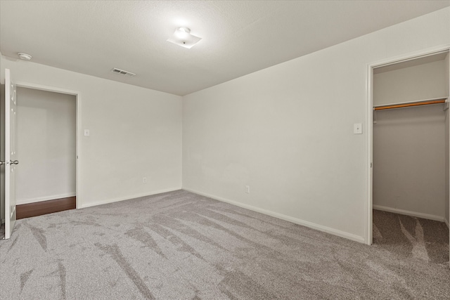 unfurnished bedroom featuring a textured ceiling, carpet floors, a spacious closet, and a closet