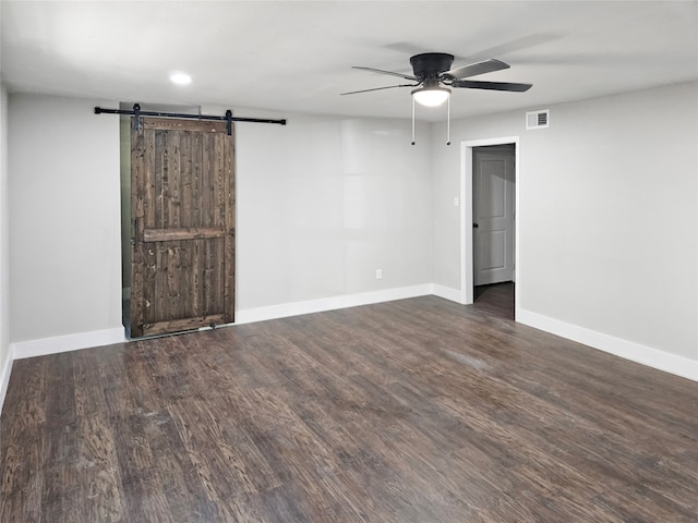 empty room with a barn door, ceiling fan, and dark hardwood / wood-style flooring