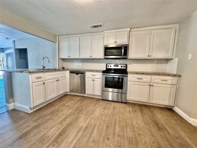 kitchen featuring stone countertops, appliances with stainless steel finishes, light hardwood / wood-style floors, sink, and white cabinets