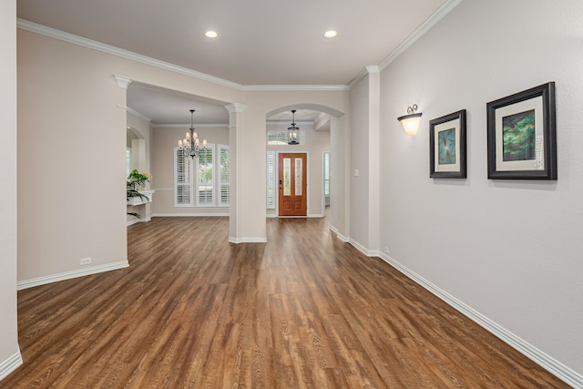 empty room featuring decorative columns, crown molding, dark hardwood / wood-style flooring, and a chandelier