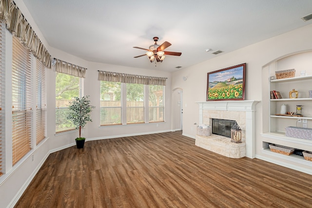 unfurnished living room featuring wood-type flooring, ceiling fan, a tile fireplace, and built in features