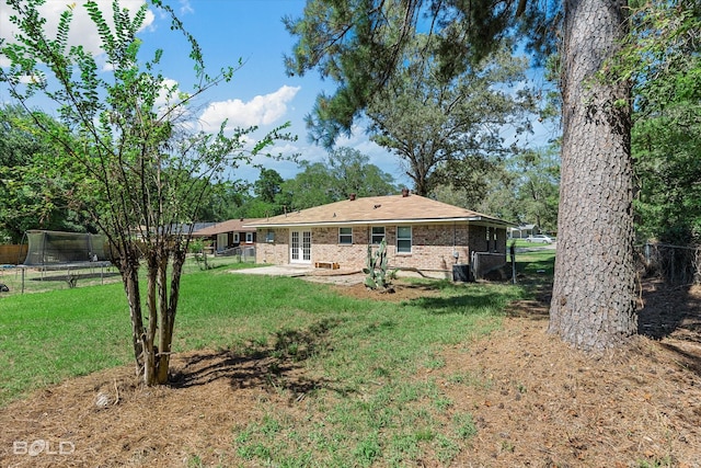 back of property with a trampoline, a yard, and a patio area