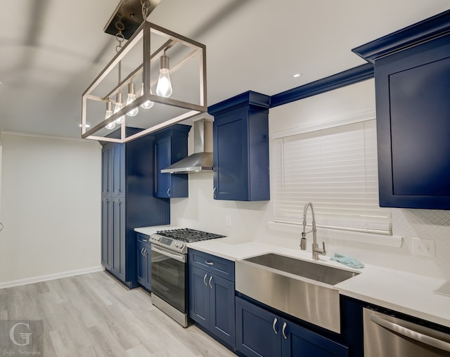 kitchen with ornamental molding, wall chimney range hood, stainless steel appliances, and blue cabinetry