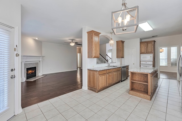 kitchen featuring white microwave, a tiled fireplace, light hardwood / wood-style flooring, ceiling fan with notable chandelier, and pendant lighting