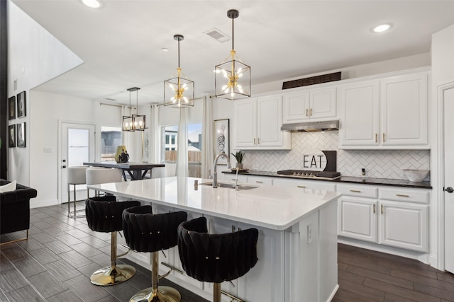 kitchen with dark hardwood / wood-style flooring, a kitchen island with sink, sink, white cabinets, and hanging light fixtures