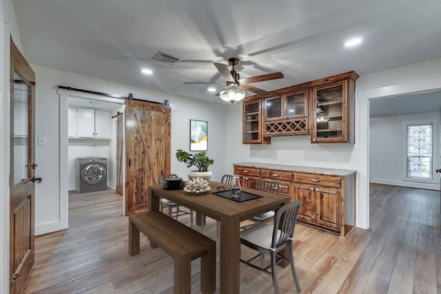 dining space with a barn door, ceiling fan, light wood-type flooring, and washer / clothes dryer