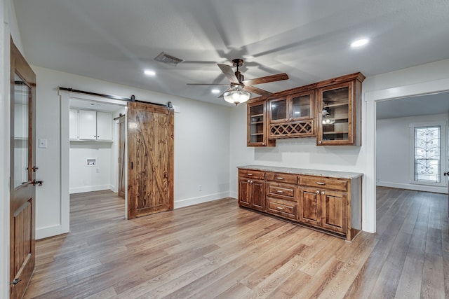 kitchen with ceiling fan, a barn door, and light hardwood / wood-style floors