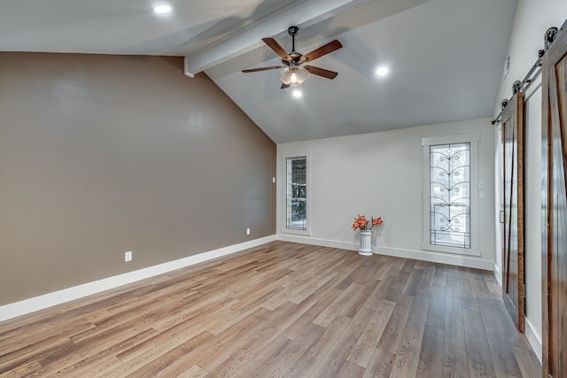 interior space featuring a barn door, ceiling fan, light wood-type flooring, and lofted ceiling with beams