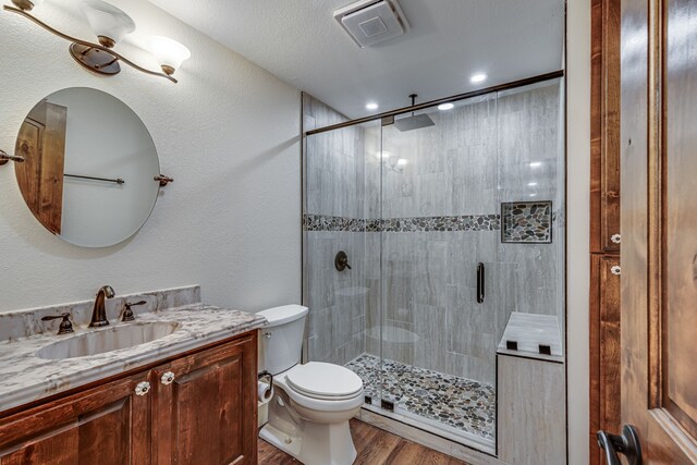 bathroom featuring hardwood / wood-style flooring, vanity, toilet, a shower with shower door, and a textured ceiling