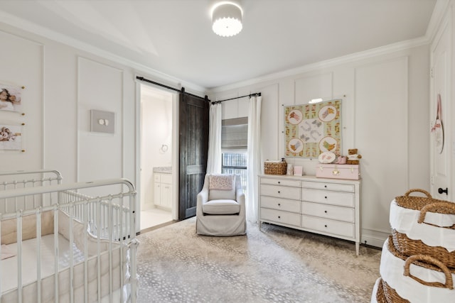 bedroom featuring ensuite bathroom, a barn door, crown molding, and a nursery area