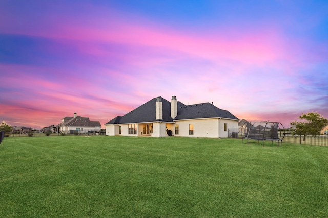 back house at dusk with a lawn and a trampoline