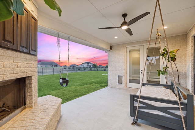 patio terrace at dusk featuring a lawn, an outdoor stone fireplace, and ceiling fan