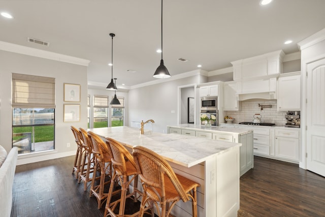 kitchen featuring decorative light fixtures, a breakfast bar area, a kitchen island with sink, white cabinets, and appliances with stainless steel finishes