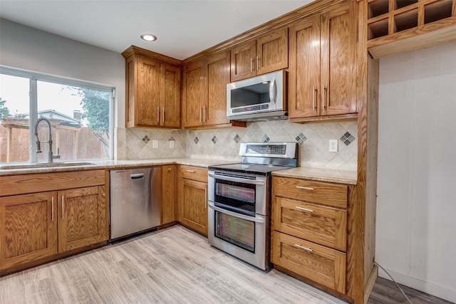 kitchen featuring backsplash, sink, light stone countertops, light wood-type flooring, and stainless steel appliances