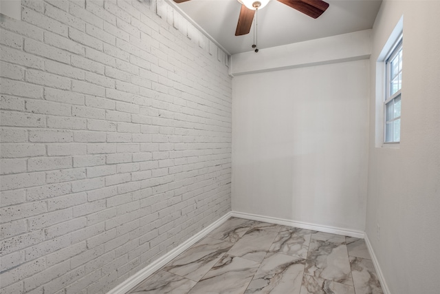 unfurnished room featuring ceiling fan and brick wall