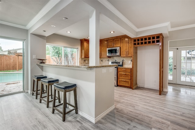 kitchen with stainless steel appliances, ornamental molding, and light hardwood / wood-style floors