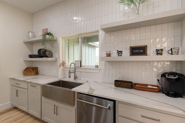 kitchen with light stone countertops, decorative backsplash, stainless steel dishwasher, sink, and light hardwood / wood-style floors