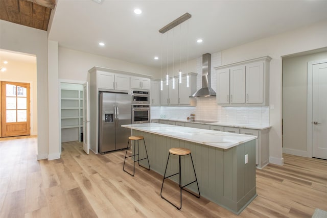 kitchen with decorative backsplash, appliances with stainless steel finishes, wall chimney exhaust hood, a kitchen island, and hanging light fixtures