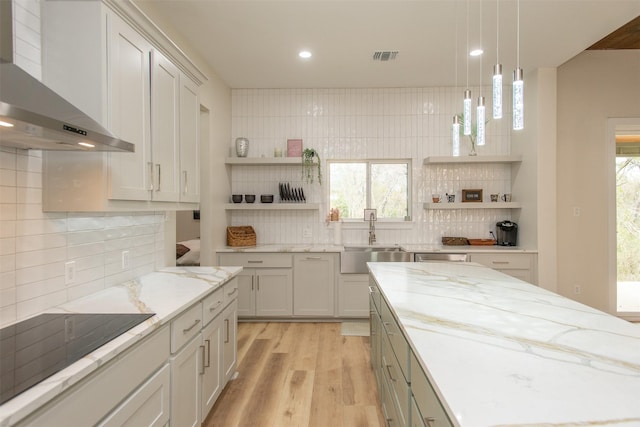 kitchen with sink, wall chimney range hood, black electric cooktop, decorative backsplash, and light wood-type flooring