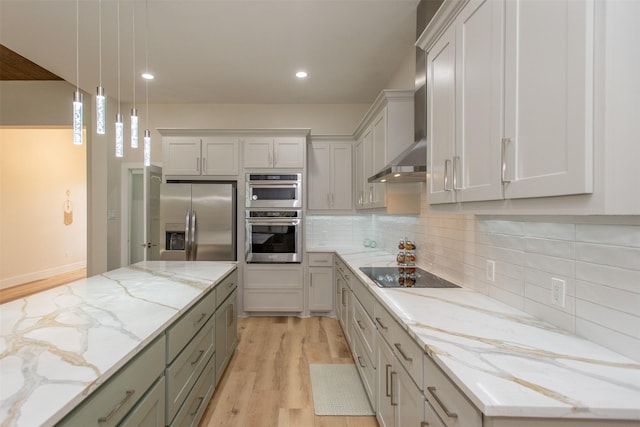 kitchen featuring appliances with stainless steel finishes, light wood-type flooring, light stone counters, wall chimney exhaust hood, and hanging light fixtures