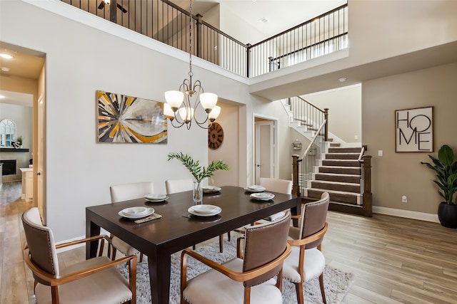 dining space with a notable chandelier, a towering ceiling, and light wood-type flooring