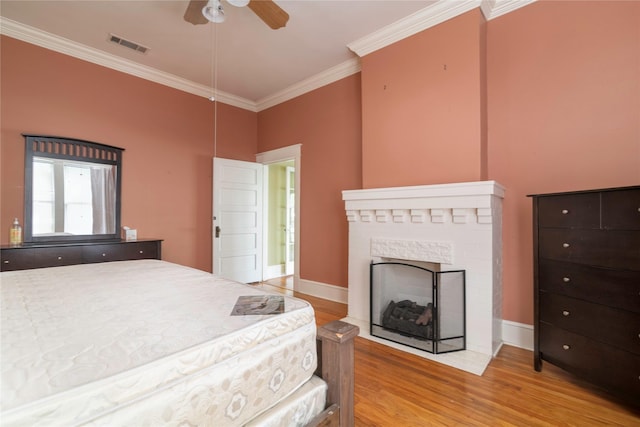 bedroom with ceiling fan, a stone fireplace, light wood-type flooring, and crown molding