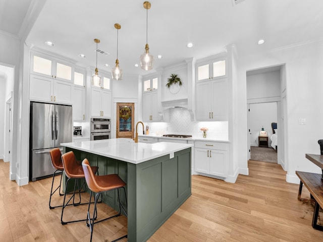 kitchen featuring a center island with sink, stainless steel appliances, decorative backsplash, light countertops, and white cabinets