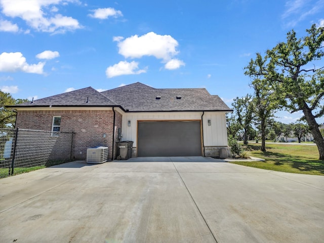 view of front facade with cooling unit, fence, a shingled roof, a garage, and brick siding