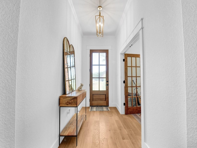 entryway featuring ornamental molding, light wood-style floors, baseboards, a chandelier, and a textured wall