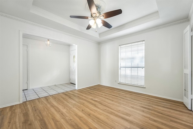 unfurnished bedroom featuring ceiling fan, ornamental molding, light wood-type flooring, and a tray ceiling