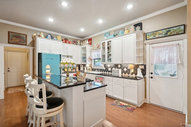 kitchen with crown molding, light hardwood / wood-style flooring, a kitchen island, white cabinetry, and a breakfast bar area