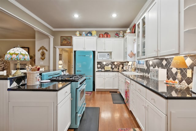 kitchen with light wood-type flooring, gas stove, white microwave, sink, and white cabinets