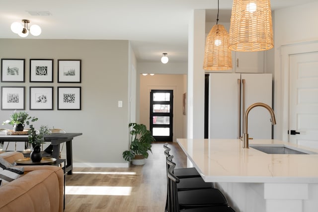 kitchen featuring white fridge, light stone countertops, hardwood / wood-style floors, hanging light fixtures, and sink