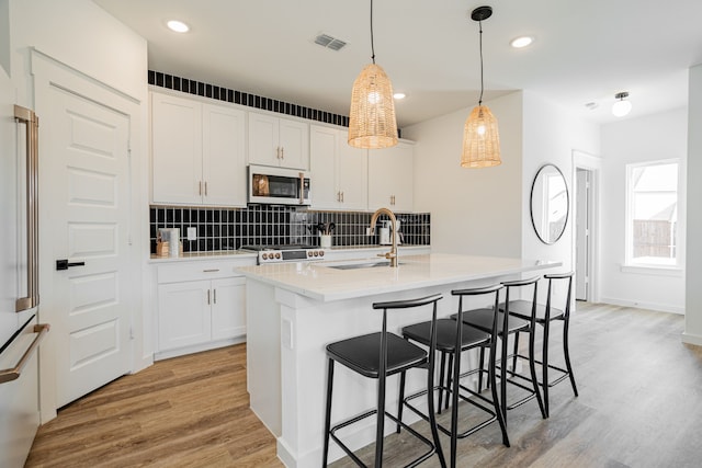 kitchen featuring appliances with stainless steel finishes, a center island with sink, light hardwood / wood-style floors, and white cabinetry