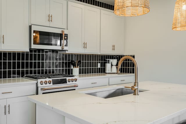 kitchen with hanging light fixtures, gas stove, light stone countertops, white cabinetry, and sink