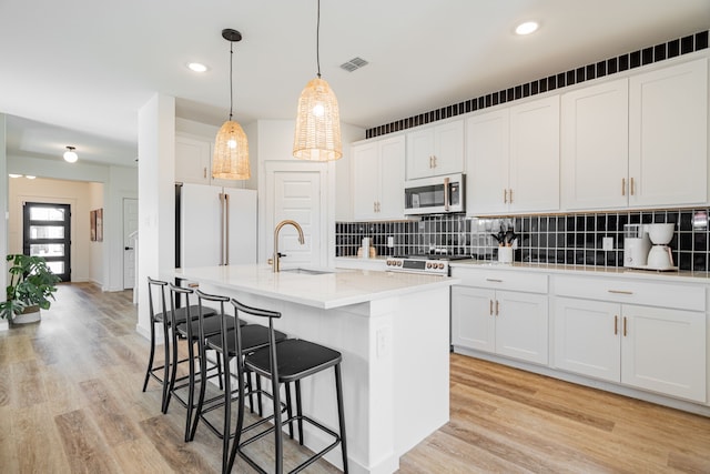 kitchen with light hardwood / wood-style flooring, stainless steel appliances, a kitchen island with sink, and white cabinetry