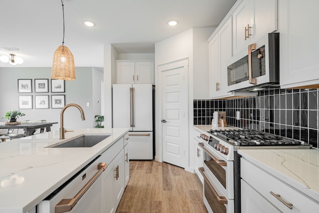 kitchen featuring appliances with stainless steel finishes, light hardwood / wood-style floors, white cabinetry, sink, and pendant lighting