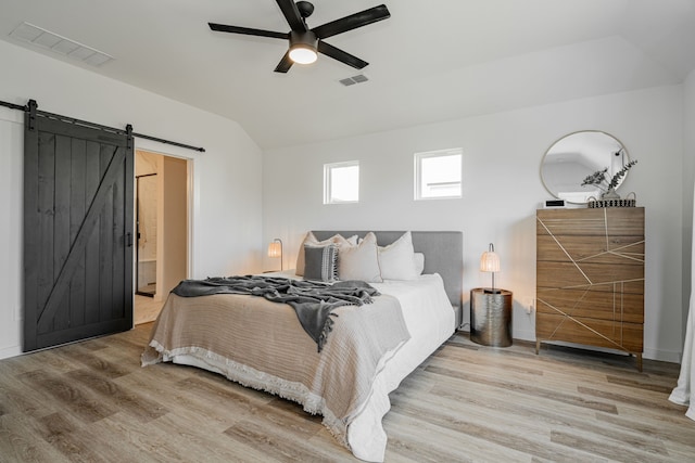 bedroom featuring light wood-type flooring, lofted ceiling, ceiling fan, and a barn door