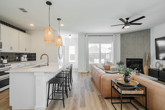 kitchen featuring a tiled fireplace, decorative light fixtures, light hardwood / wood-style flooring, an island with sink, and sink