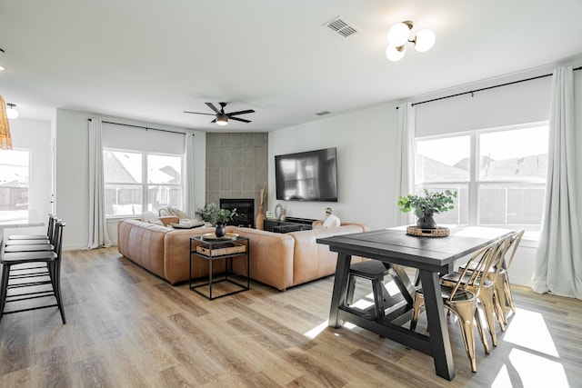 living room with a tiled fireplace, light wood-type flooring, and ceiling fan