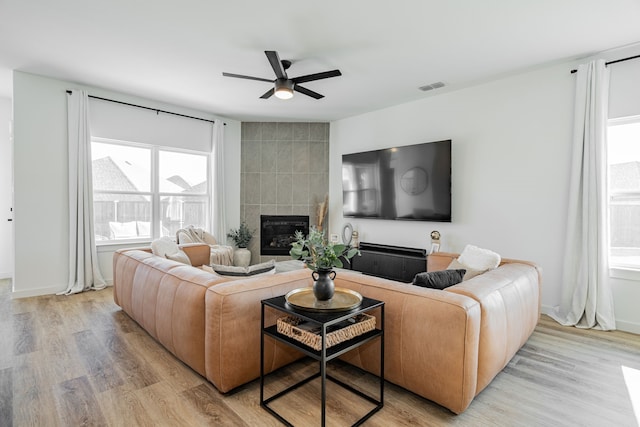 living room with a fireplace, a healthy amount of sunlight, ceiling fan, and light hardwood / wood-style floors